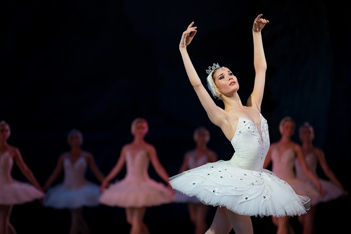 Prima ballerina white swan on stage dancing gracefully against other dancers. Ballet Swan Lake, the Opera House in Kiev, Ukraine.